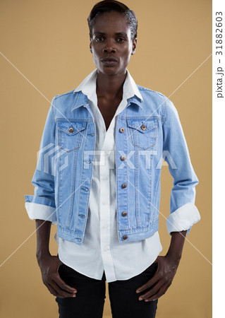 Androgynous man in denim jacket posing against beige background 31882603