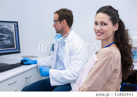 Female patient smiling at camera while dentist looking at an x-ray 31882641