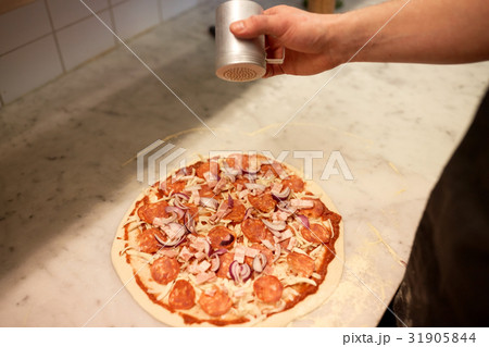 cook adding pepper to salami pizza at pizzeria cook adding pepper to salami pizza at pizzeria 31905844