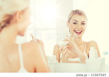happy woman applying cream to face at bathroom 31907685