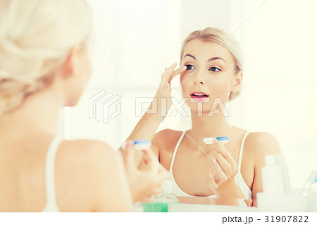 young woman putting on contact lenses at bathroom young woman putting on contact lenses at bathroom 31907822