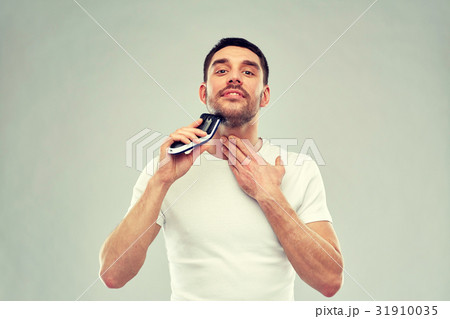 smiling man shaving beard with trimmer over gray smiling man shaving beard with trimmer over gray 31910035
