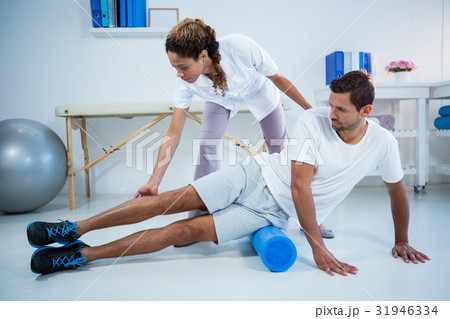 Physiotherapist doing leg therapy to a man using foam roll Physiotherapist doing leg therapy to a man using foam roll 31946334