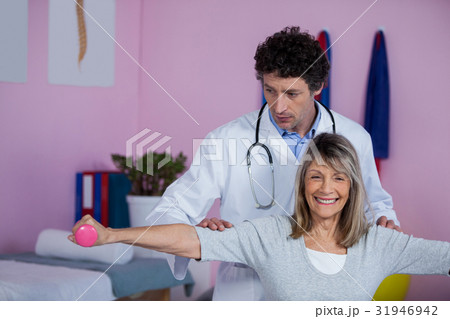 Physiotherapist assisting senior woman to lift dumbbell Physiotherapist assisting senior woman to lift dumbbell 31946942