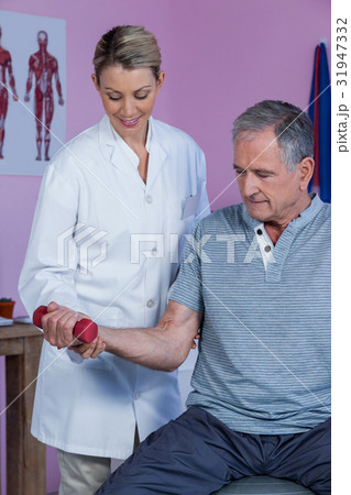 Physiotherapist assisting senior man to lift dumbbell Physiotherapist assisting senior man to lift dumbbell 31947332
