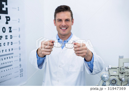 Smiling optometrist holding spectacles Smiling optometrist holding spectacles 31947369