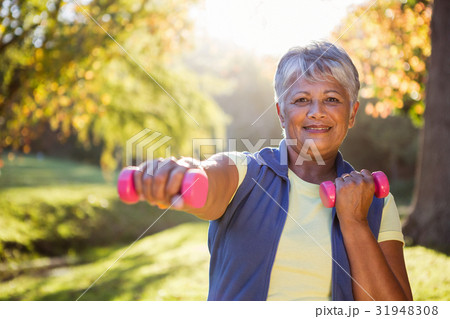 Smiling mature woman exercising with dumbbell Smiling mature woman exercising with dumbbell 31948308