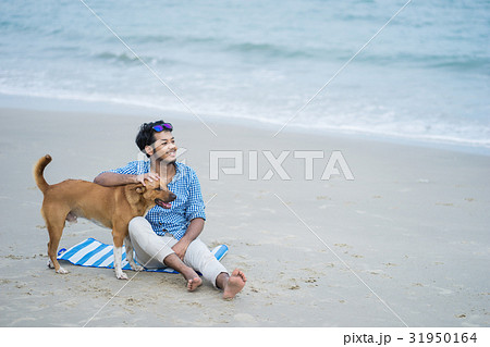 A happy man is sitting and touching a dog on the beach A happy man is sitting and touching a dog on the beach 31950164