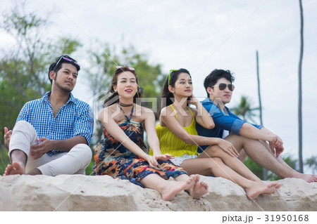 Four friends are sitting on sandy shore and looking something 31950168