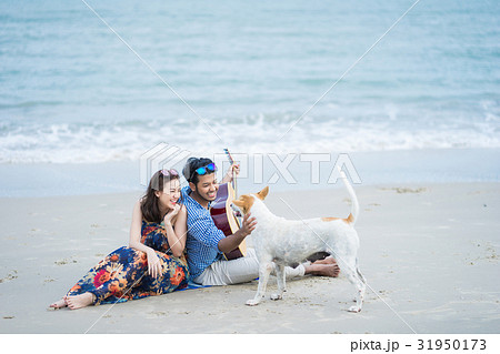 A couple is sitting, playing with their dog and smiling happily. 31950173