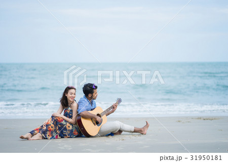 Picture of a happy couple sitting and playing guitar on the beach 31950181