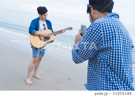 A man is taking photo for his friend standing, playing guitar on the beach 31950188