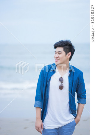 a man is standing, smiling and looking at something on the beach a man is standing, smiling and looking at something on the beach 31950227