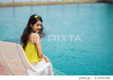 A young beautiful girl is sitting near a pool and smiling. A young beautiful girl is sitting near a pool and smiling. 31950306