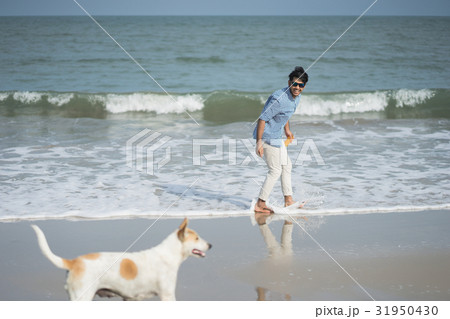 A photo of a man smiling and looking at a dog on the beach. 31950430