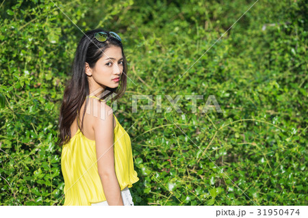 a photo of an Asian woman standing near bushes and looking back 31950474
