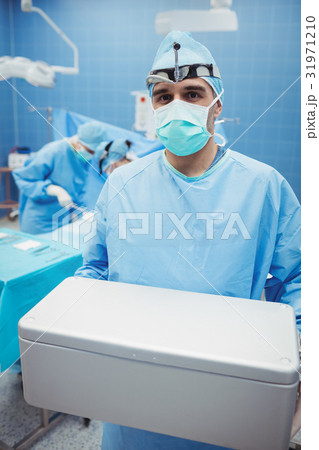 Portrait of surgeon holding ice box while colleagues performing operation 31971210