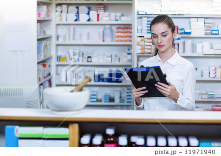 Pharmacist looking in clipboard at counter Pharmacist looking in clipboard at counter 31971940