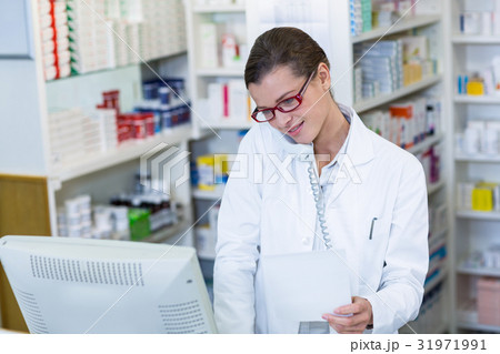 Pharmacist holding prescription paper while talking on phone Pharmacist holding prescription paper while talking on phone 31971991