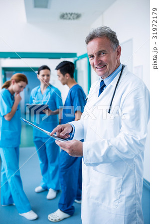 Portrait of smiling doctor standing with x-ray report in corridor Portrait of smiling doctor standing with x-ray report in corridor 31972179