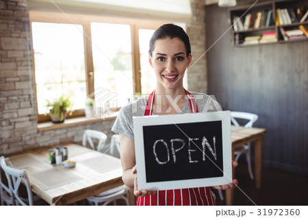 Portrait of female baker holding open signboard 31972360