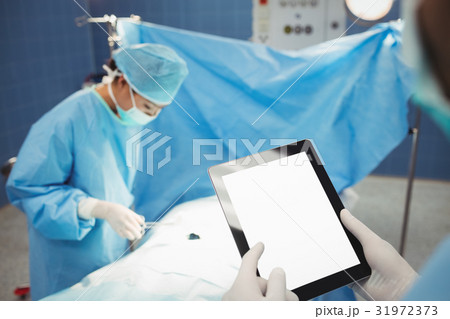 Surgeon using digital while nurse operating patient in operation room Surgeon using digital while nurse operating patient in operation room 31972373