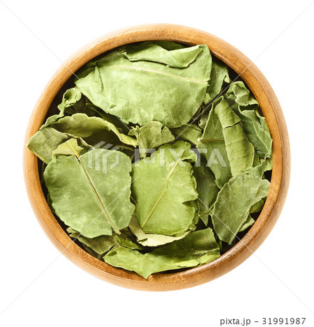 Dried kaffir lime leaves in wooden bowl over white Dried kaffir lime leaves in wooden bowl over white 31991987