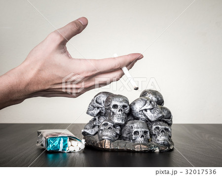 Male hand holding cigarette, skulls on table Male hand holding cigarette, skulls on table 32017536