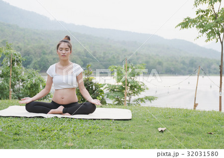 asian pregnant woman practicing yoga while sitting on green grass in public park. meditating on maternity. concept of healthy lifestyle and relaxation. asian pregnant woman practicing yoga while sitting on green grass in public park. meditating on maternity. concept of healthy lifestyle and relaxation. 32031580