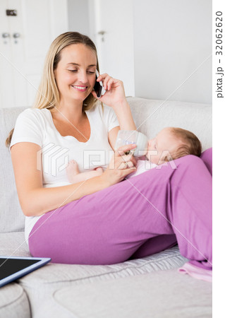 Mother talking on mobile phone while feeding her baby with milk bottle 32062620