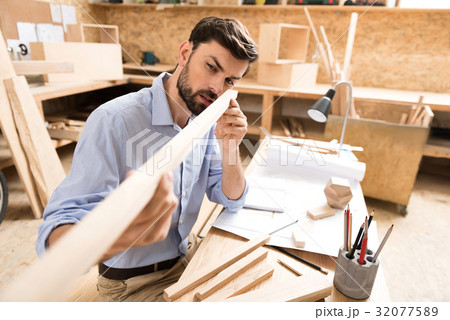 Concentrated bearded youthful woodworker checking Concentrated bearded youthful woodworker checking 32077589