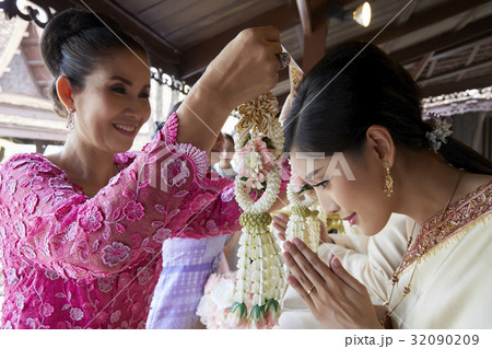 A woman in pink dress is preparing to put garland on the bride's neck A woman in pink dress is preparing to put garland on the bride's neck 32090209