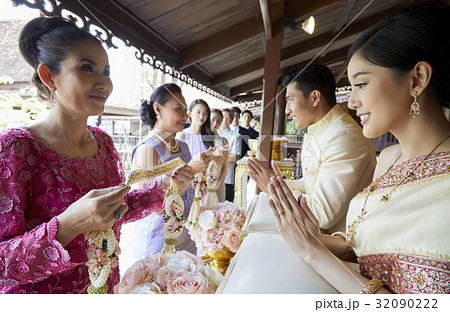 Two women are holding garland while the groom and bride are looking at it. Two women are holding garland while the groom and bride are looking at it. 32090222