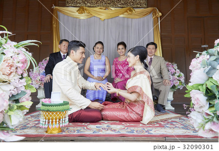 bride is wearing a ring into groom's finger in front of their parents. bride is wearing a ring into groom's finger in front of their parents. 32090301