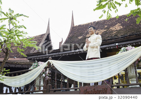 A groom is standing, smiling and praying in the balcony. 32090440