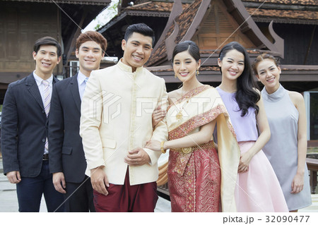 A groom and a bride are smiling and standing beside their friends 32090477