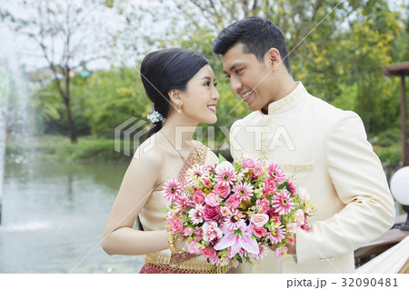A happy couple is holding flowers and smiling beside the lake 32090481