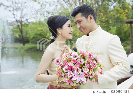 A happy couple is holding flowers and looking at each other near a lake 32090482