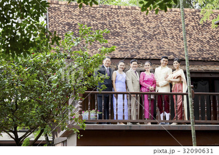 a couple are standing outside of the house with their parents. 32090631