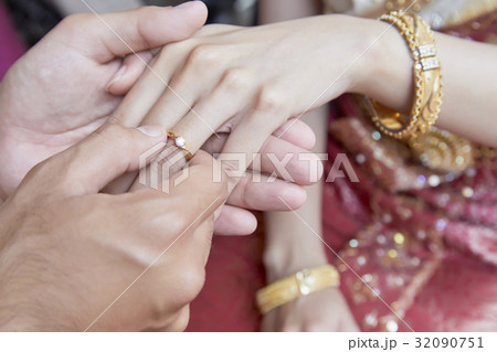 the groom is holding the hand of the bride and putting the ring on. 32090751