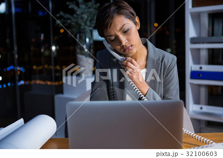 Businesswoman talking on phone while working in office Businesswoman talking on phone while working in office 32100603