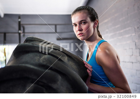 Portrait of female athlete pushing tire in gym 32100849