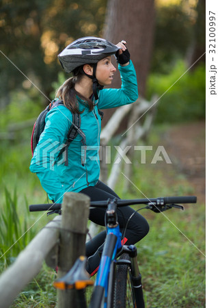 Female biker sitting on a fence in countryside Female biker sitting on a fence in countryside 32100997