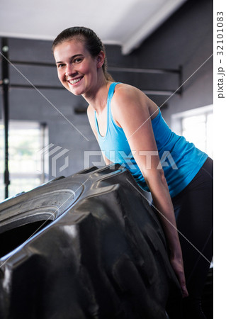 Portrait of smiling female athlete pushing tire in gym Portrait of smiling female athlete pushing tire in gym 32101083