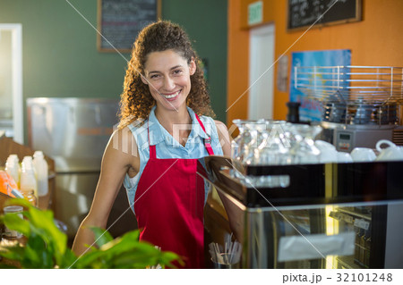 Portrait of smiling female staff standing at coffee shop counter 32101248