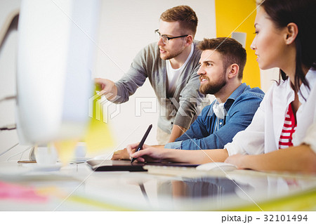 Executive pointing at computer monitor to colleagues in creative office 32101494