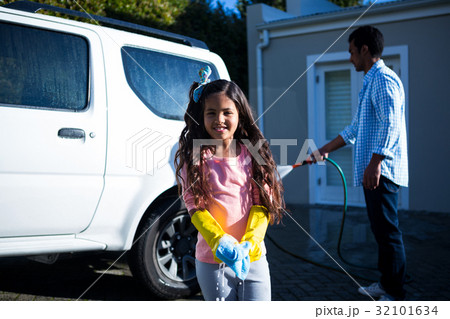 Daughter holding sponge while father doing carwash 32101634