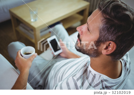 Father using phone while having coffee in living room Father using phone while having coffee in living room 32102019