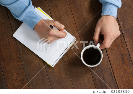 Man holding a cup of coffee and writing on notepad 32102330
