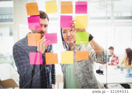 Creative business people looking at multi colored sticky notes on glass 32104331